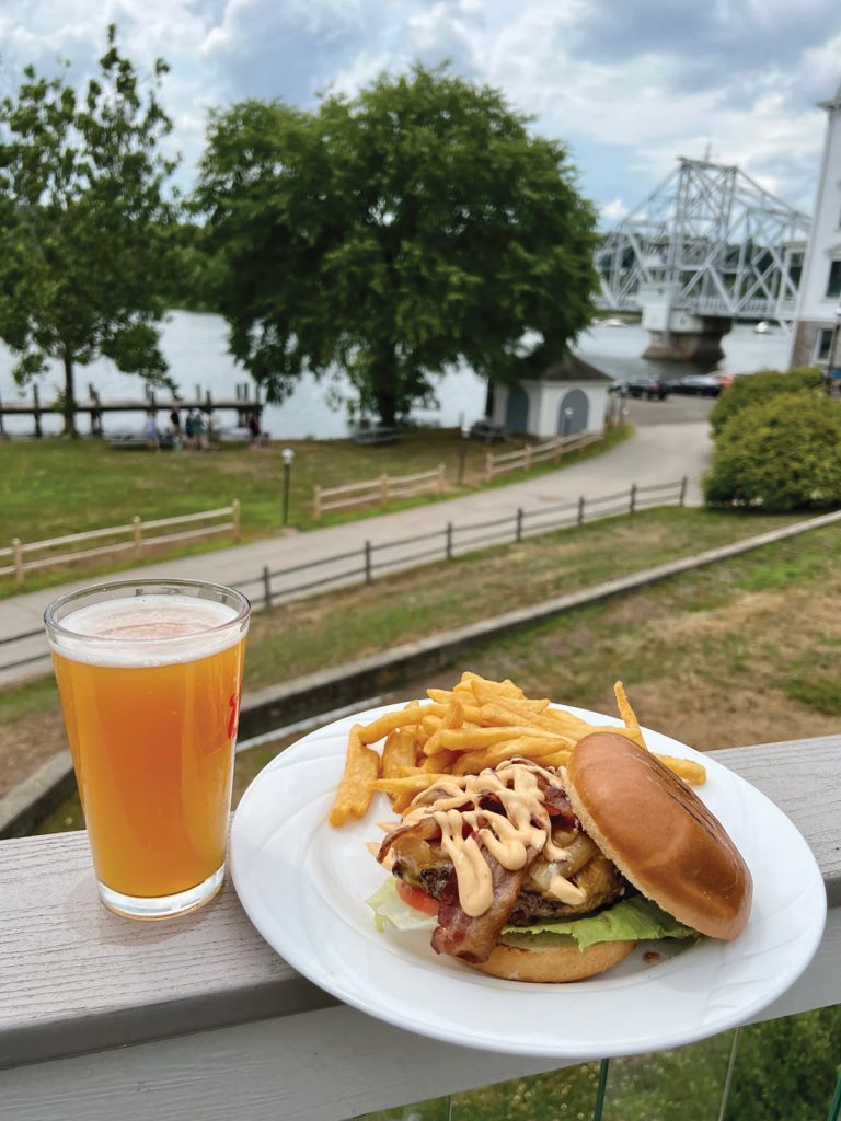 burger and drink on railing with river and bridge in background