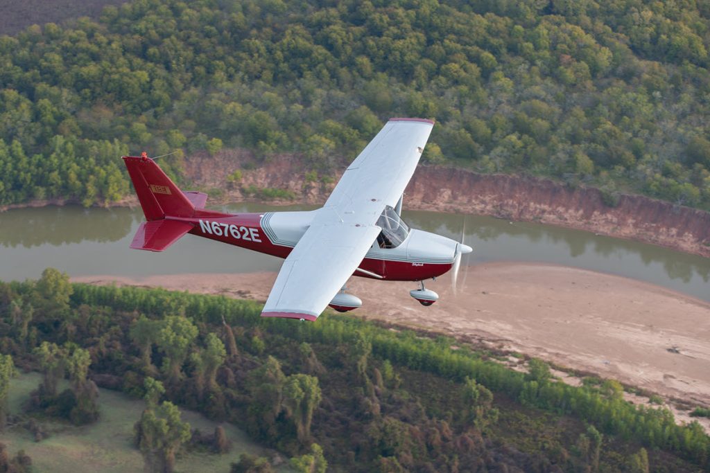 top view of white and red cessna skylark in flight over river